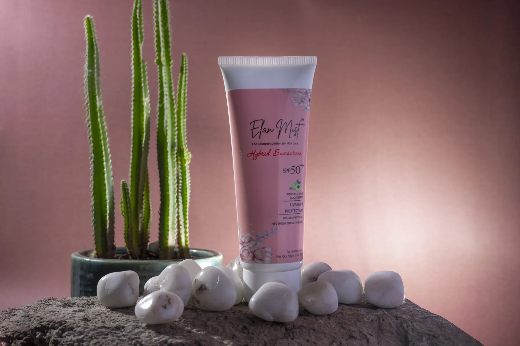 Elanmist Hybrid Sunscreen tube on a rock beside a potted cactus and white pebbles